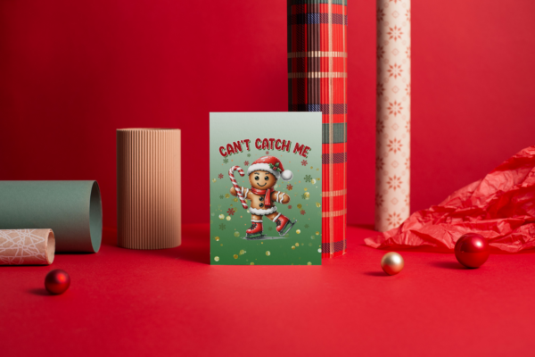 A cute gingerbread man ice skating with a candy cane holiday greeting card. Card is sitting in front of Christmas wrapping paper.