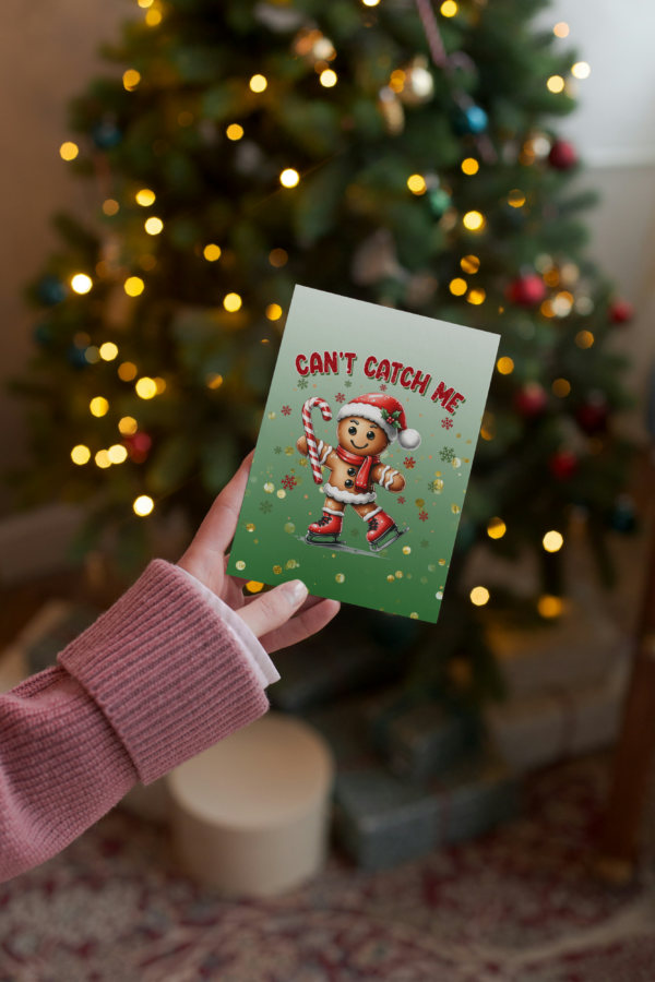 A cute gingerbread man ice skating with a candy cane holiday greeting card. Card is sitting in front of Christmas wrapping paper.