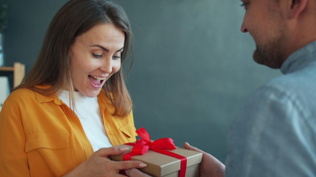 A woman with a excited expression after receiving a gift from a man.
